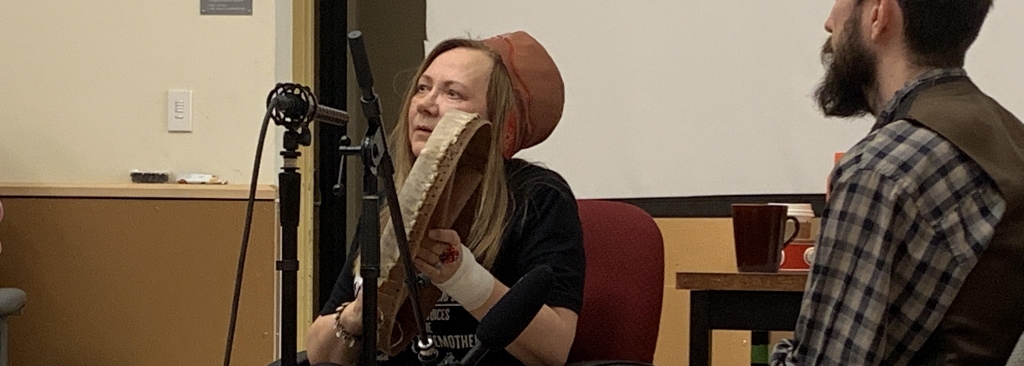 Mari Boine sits with a drum in front of a microphone.