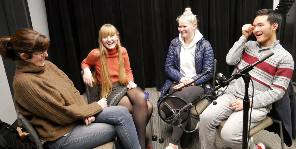 Left to right: Assitant professor Amanda Doxtater and undergraduate students Blue Palmer, Fanny Metsä-Tokila, and Bill Cheung-Daihe sit around a microphone in the studio.