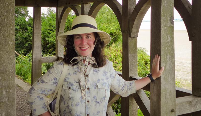 Lauren Poyer smiles in a sun hat at the end of Hadrian's Wall near the sea.