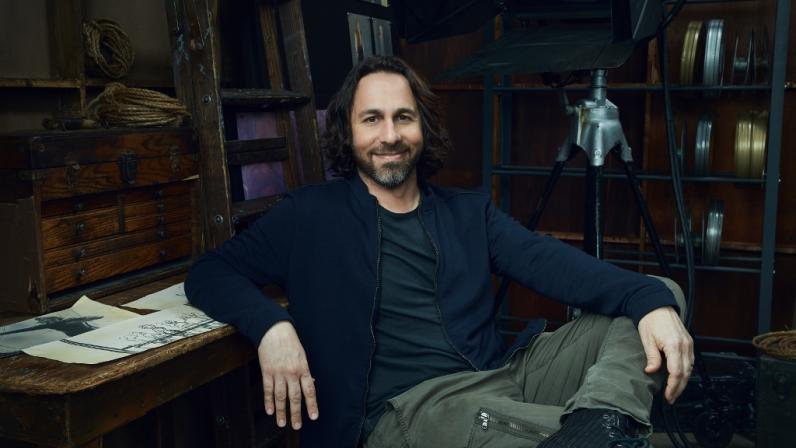 arc Smith sits in a chair next to a bookcase full of old film reels.