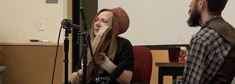 Mari Boine holds a drum and performs a song on a classroom stage.
