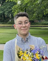subject has short brown hair and is standing smiling holding a bouquet of flowers on the Quad at UW.