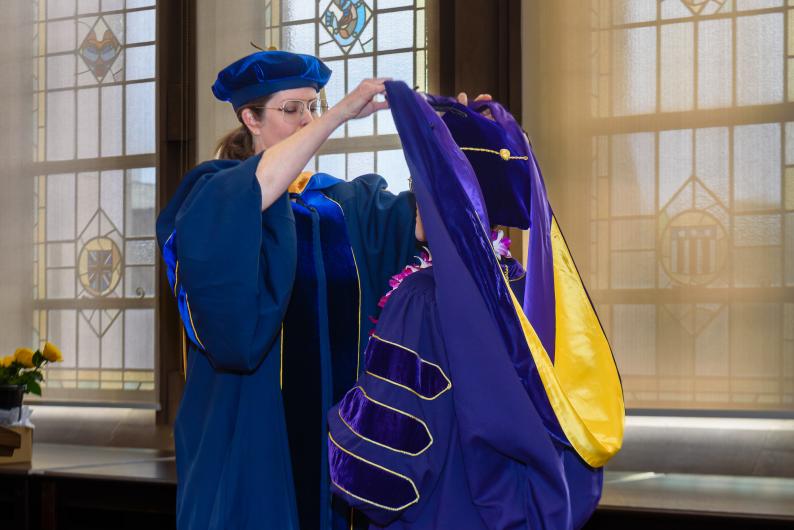 Dr. Amanda Doxtater giving the doctoral hood to a PhD graduate