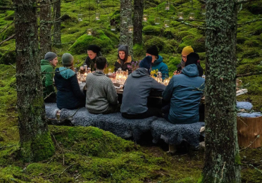 group of people seated around a candlelit table in the woods