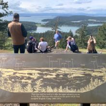 View of San Juan Islands and Canada from the top of Young Hill. Students are resting behind a map plaque of the view.