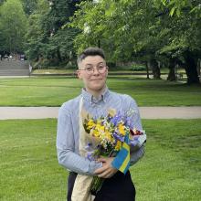 subject has short brown hair and is standing smiling holding a bouquet of flowers on the Quad at UW.