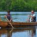 An Ojibwe elder and youth paddle a birchbark canoe together on a lake.